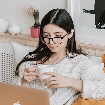 woman checking her laptop holding a cup of coffee